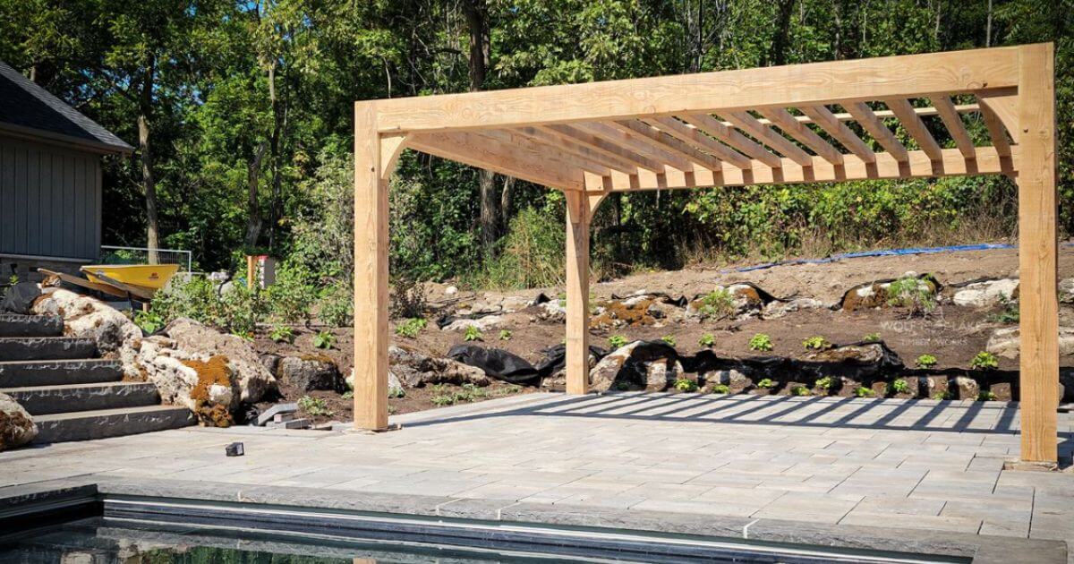 Light wood pergola beside stone patio and pool.